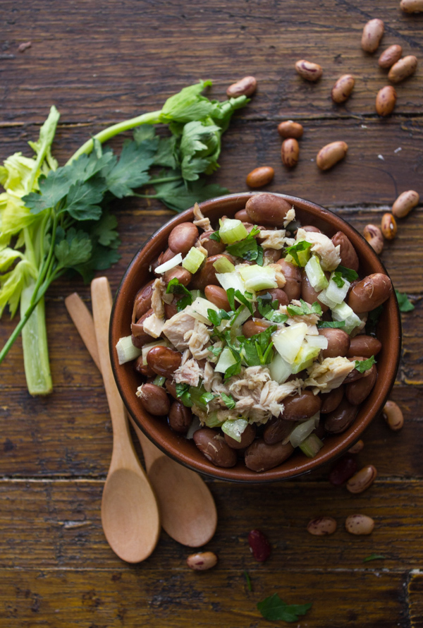 bean salad with chopped parsley on top in a brown bowl with wooden spoons