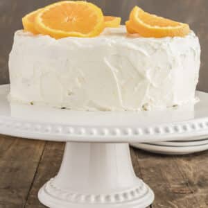 Orange cake on a white plate stand.