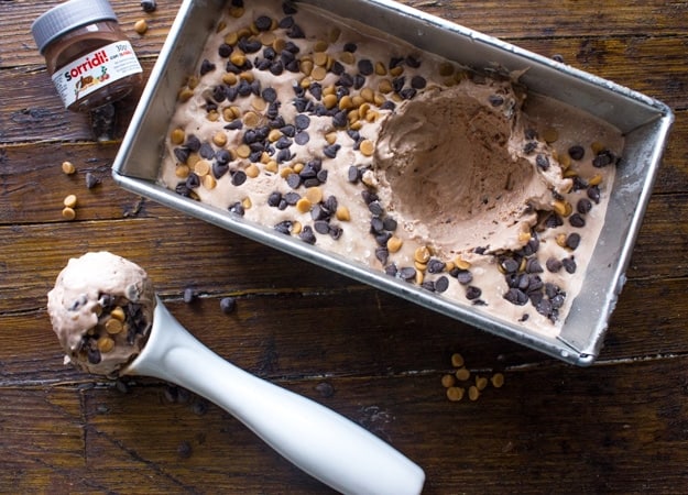 Homemade Nutella Peanut Butter Chip is an Easy No-Churn Ice in a loaf pan with a white scoop of ice cream on a wooden board.