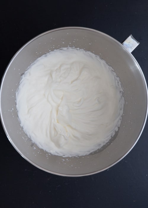 Beating the whipped cream until stiff in a silver bowl.