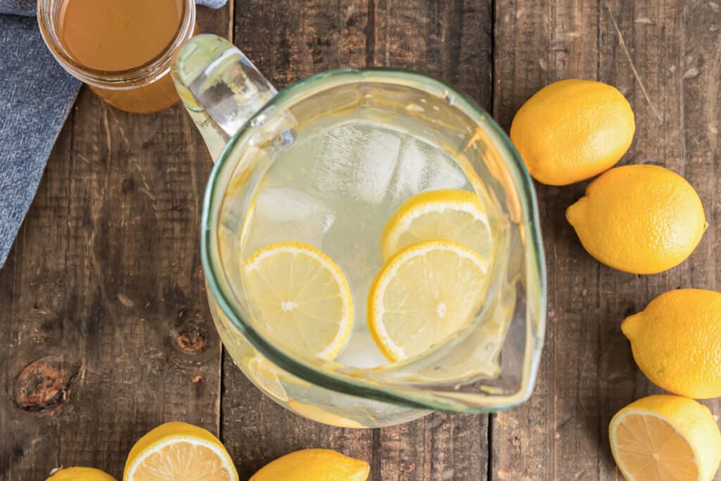 Citrus syrup drink in a jug with ice and lemon slices.