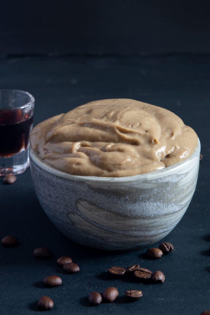 Coffee pastry cream in a grey bowl with a glass of coffee.