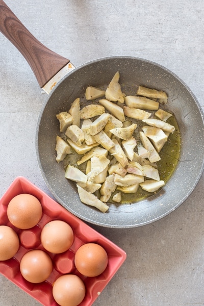 sliced artichokes in the frying pan with 6 eggs in an egg dish