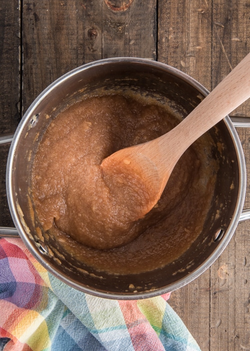 The apple butter cooked in the pot with a spoon.