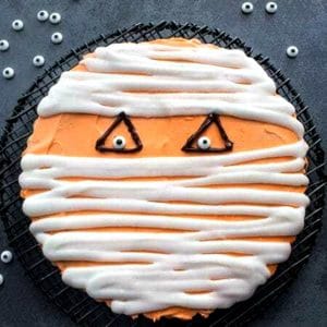 chocolate chip cookie cake mummy face on a black wire rack