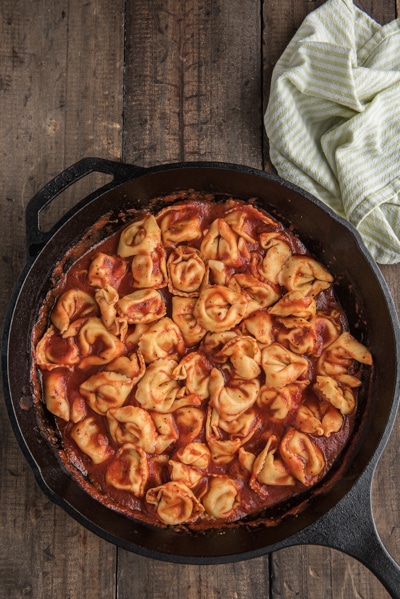 The tortellini added to the sauce in the black pan.