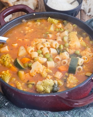 minestrone in a red pot with parmesan cheese in a small black bowl
