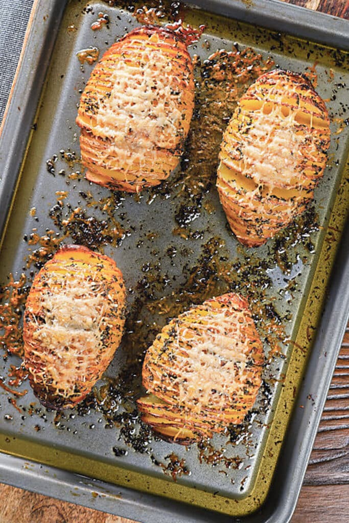 Four hasselback potatoes on a baking sheet.