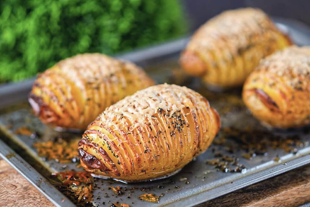 Four baked potatoes on a baking sheet.