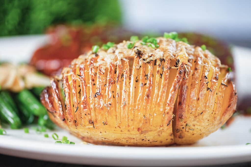 A hasselback potato on a white plate.