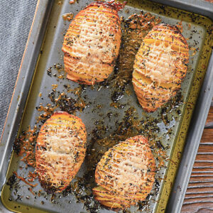 Four hasselback potatoes on a baking sheet.