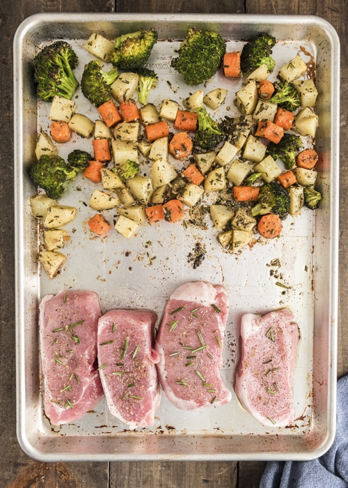 The pork chops on the baking sheet with the vegetables before cooking.