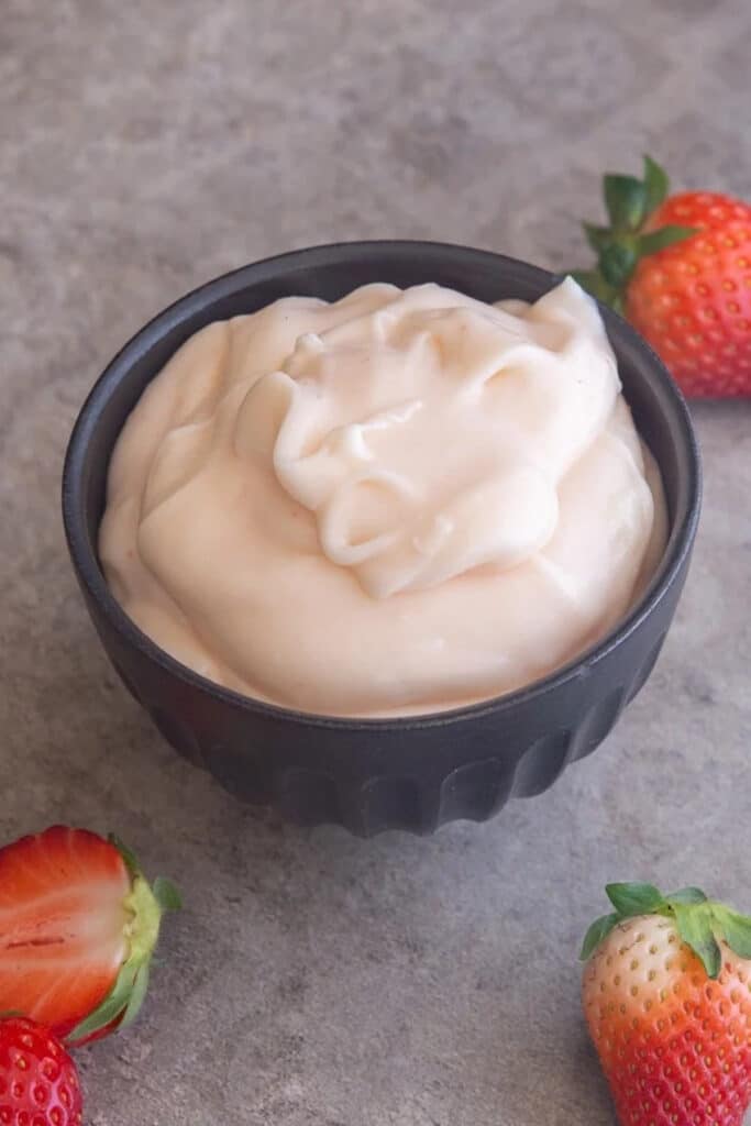 Strawberry frosting in a black bowl.