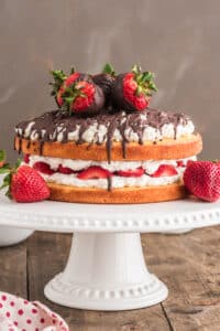 Strawberry cake on a white cake plate.