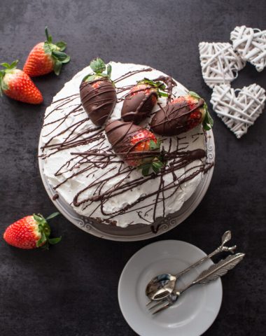 A delicious Vanilla Yogurt Cake filled with whipped cream and strawberries, topped with chocolate dipped strawberries and chocolate drizzle.