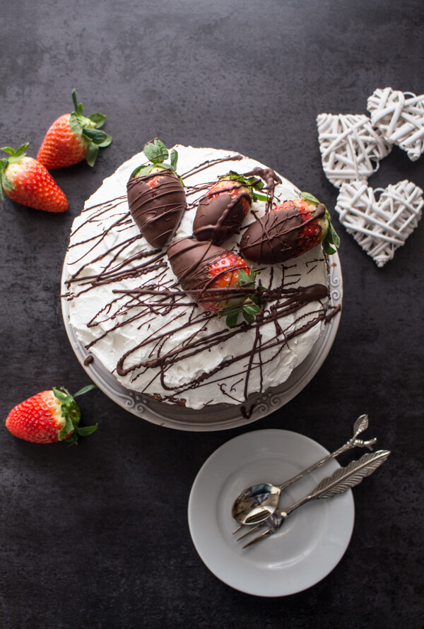 A delicious Vanilla Yogurt Cake filled with whipped cream and strawberries, topped with chocolate dipped strawberries and chocolate drizzle.