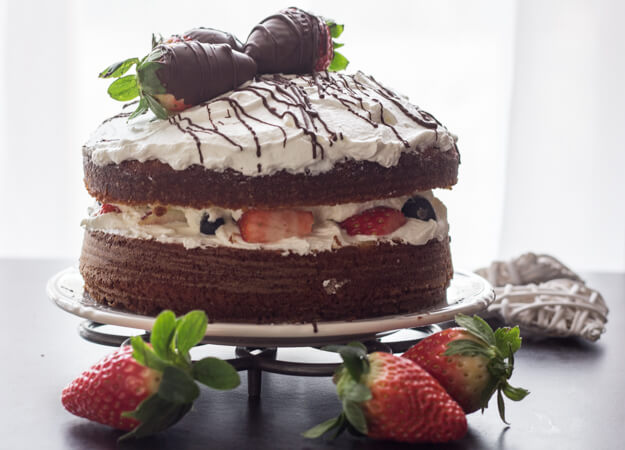 A delicious Vanilla Yogurt Cake filled with whipped cream and strawberries, topped with chocolate dipped strawberries and chocolate drizzle.