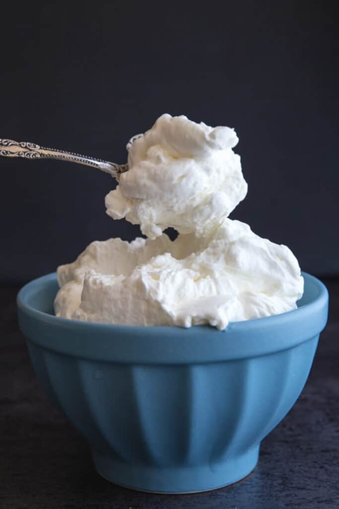 Stabilized whipped cream in a blue bowl and on a spoon.