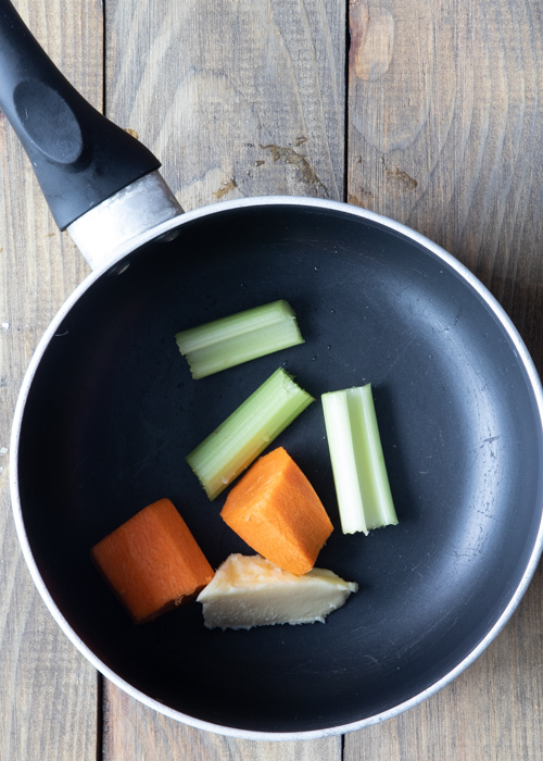 Butter, celery and carrot pieces in a black pot.