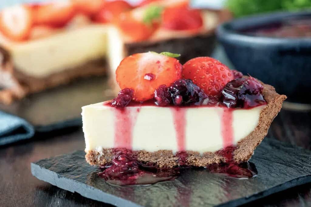 A slice of pie with berries on top, on a black plate.