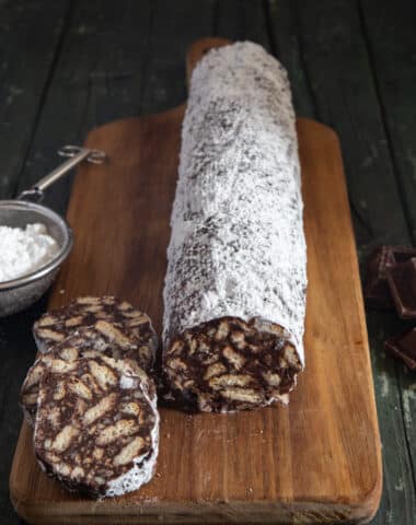 Chocolate salami on a wooden board with 3 slices cut.