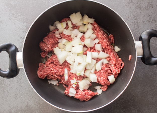 meat and chopped onion in a black pot