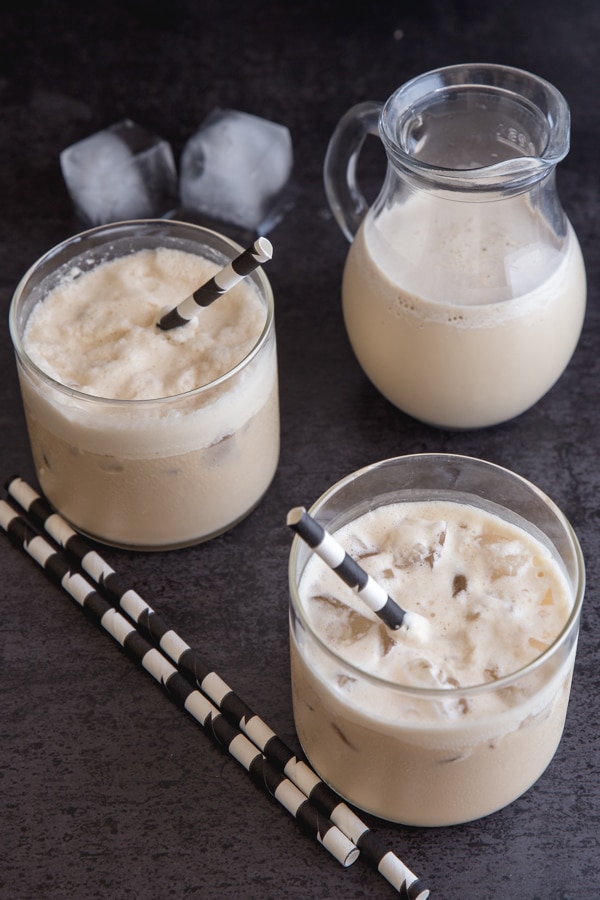 2 glasses and a jug of iced coffee on a black board with black and white straws