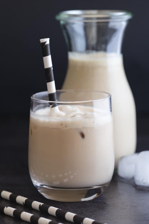 iced coffee in a glass with a black and white straw and a caraf