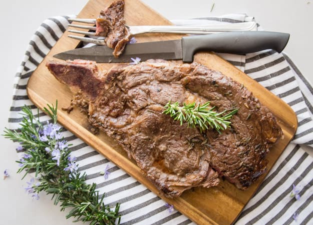 grilled steak with a piece cut on a fork with a knife sitting on a wooden board on a striped napkin