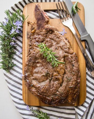 grilled marinated steak on a wooden board with sprigs of rosemary