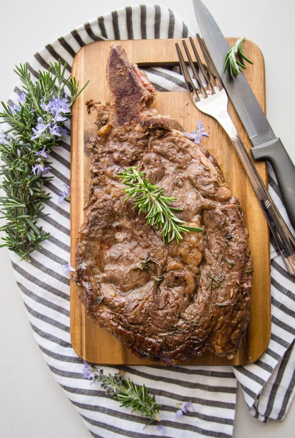 grilled marinated steak on a wooden board with sprigs of rosemary