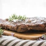 side view of grilled steak and rosemary on a wooden board