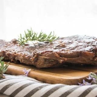 side view of grilled steak and rosemary on a wooden board