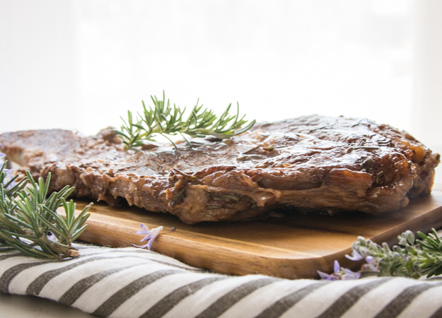 side view of grilled steak and rosemary on a wooden board