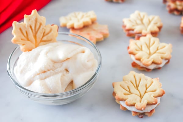 maple leaf cookies on a white board and one dipped in a glass bowl with filling
