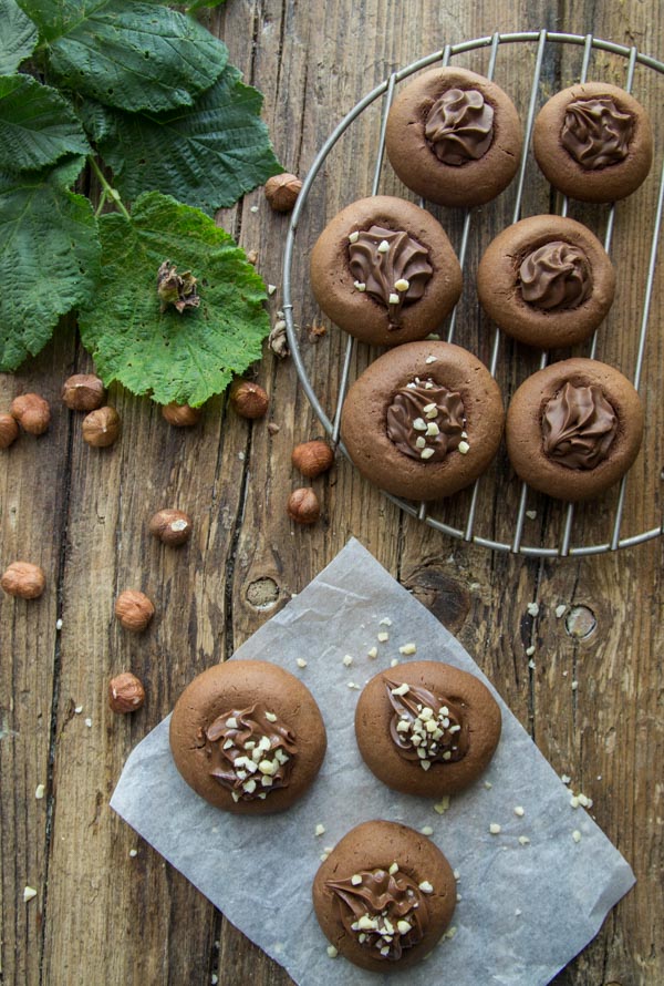 round cookies filled with nutella, on a wooden board with whole hazelnuts