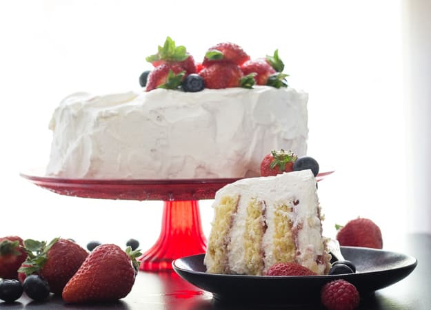 vertical layer cake on a red stand with a slice on a plate