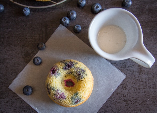 lemon glaze in a small pitcher with blueberry baked donuts and fresh blueberries