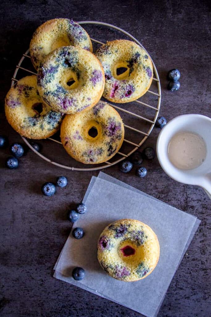 Blueberry donuts on a wire rack and one on parchment paper.