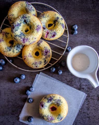 Blueberry donuts on a wire rack and one on parchment paper.