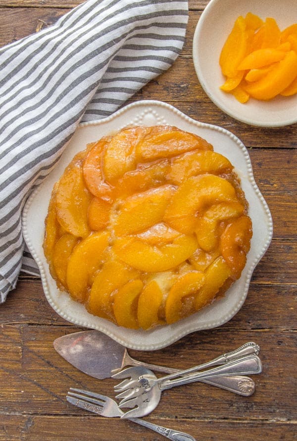 peach upside down cake on a plate with sliced peaches in a small bowl