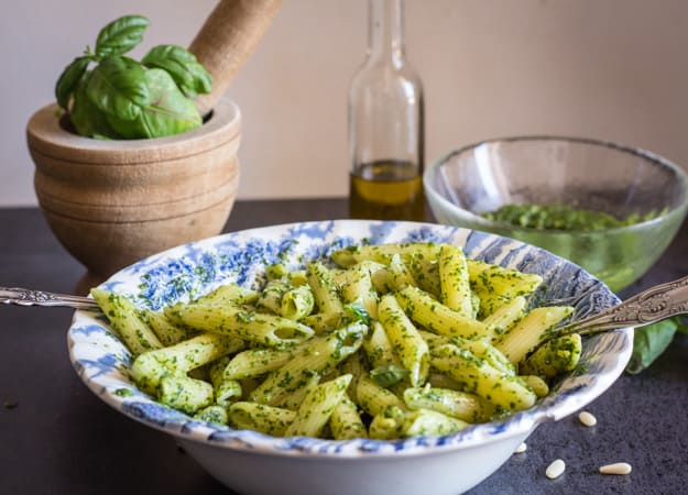 a bowl of classic basil pesto with fresh basil, olive oil in the back ground