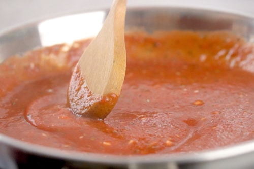 Sauce with a wooden spoon in a frying pan.
