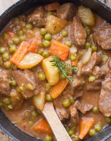 Beef stew in a pot with a wooden spoon.