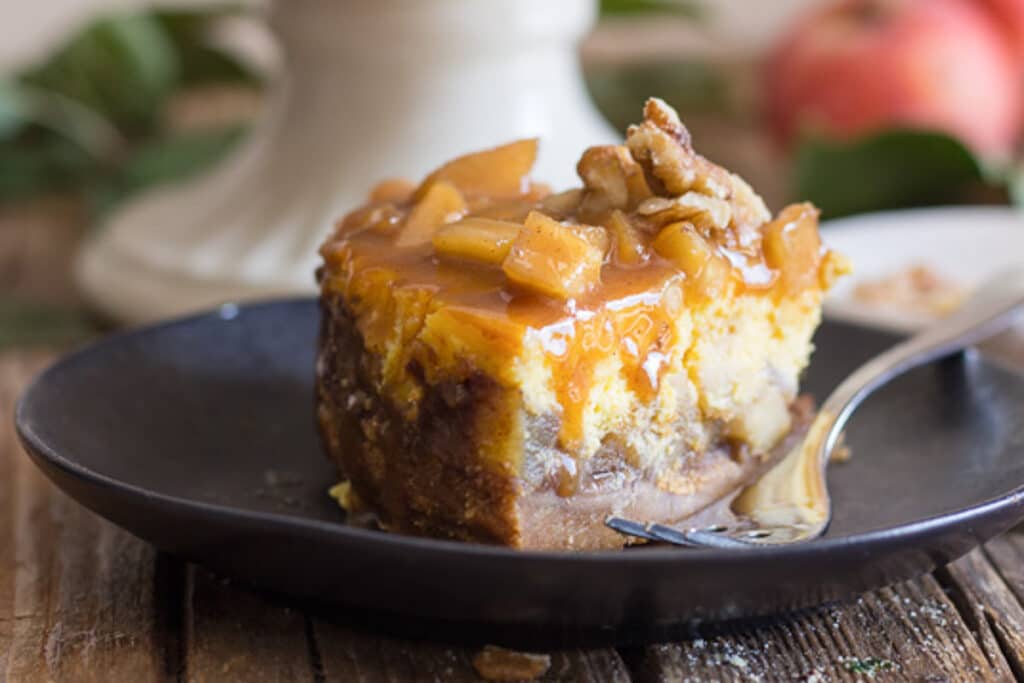 A slice of apple cheesecake on a black plate.