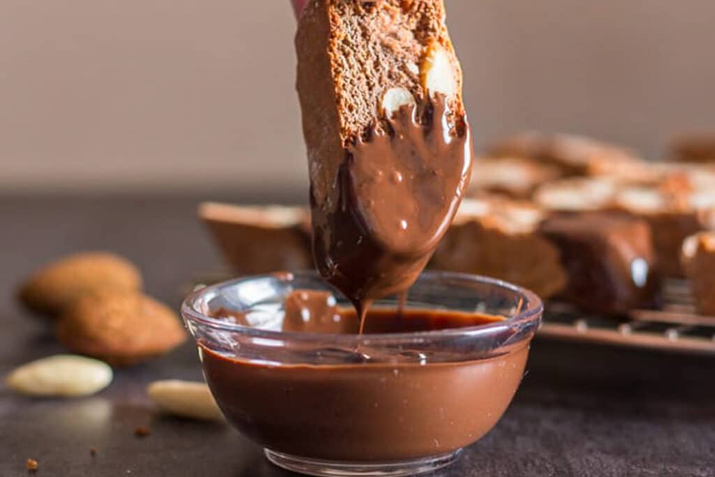 Dipping a cookie in melted chocolate.