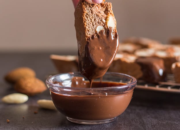 dipping a chocolate almond biscotti into melted dark chocolate