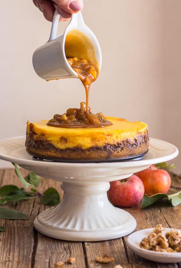 pouring maple caramel sauce from a small white jug onto the finished apple cheesecake.