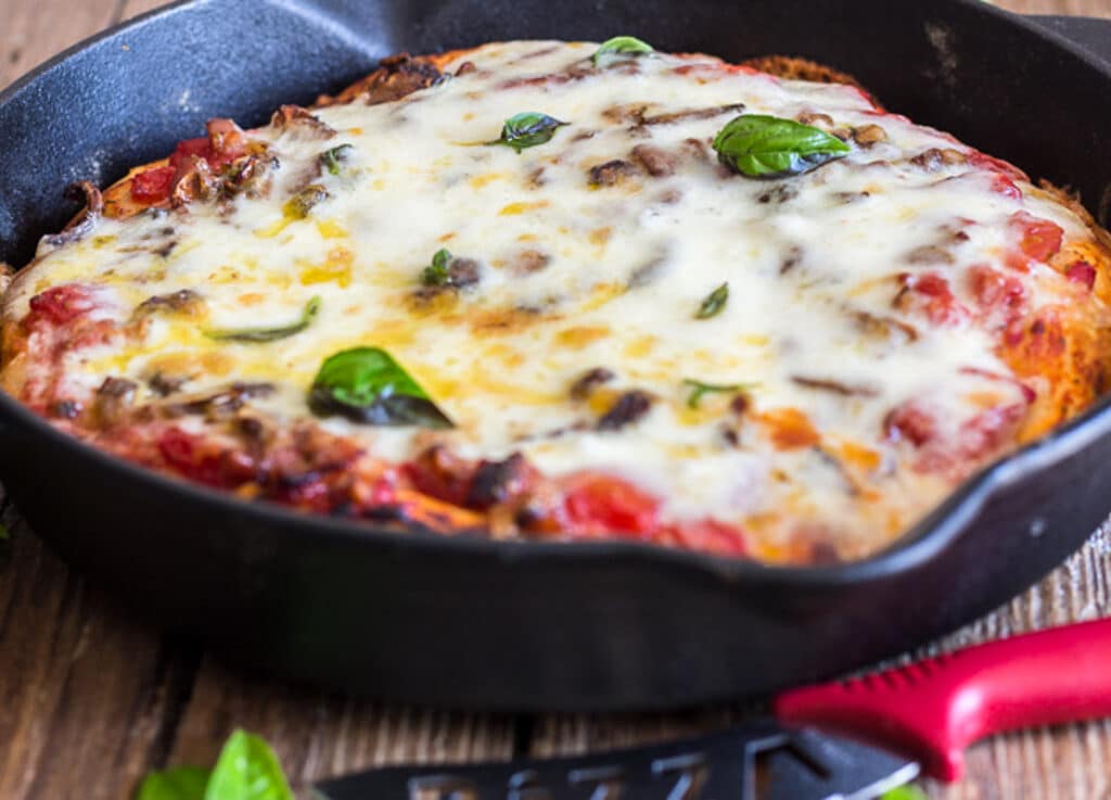Skillet pizza in the pan on a wooden board.