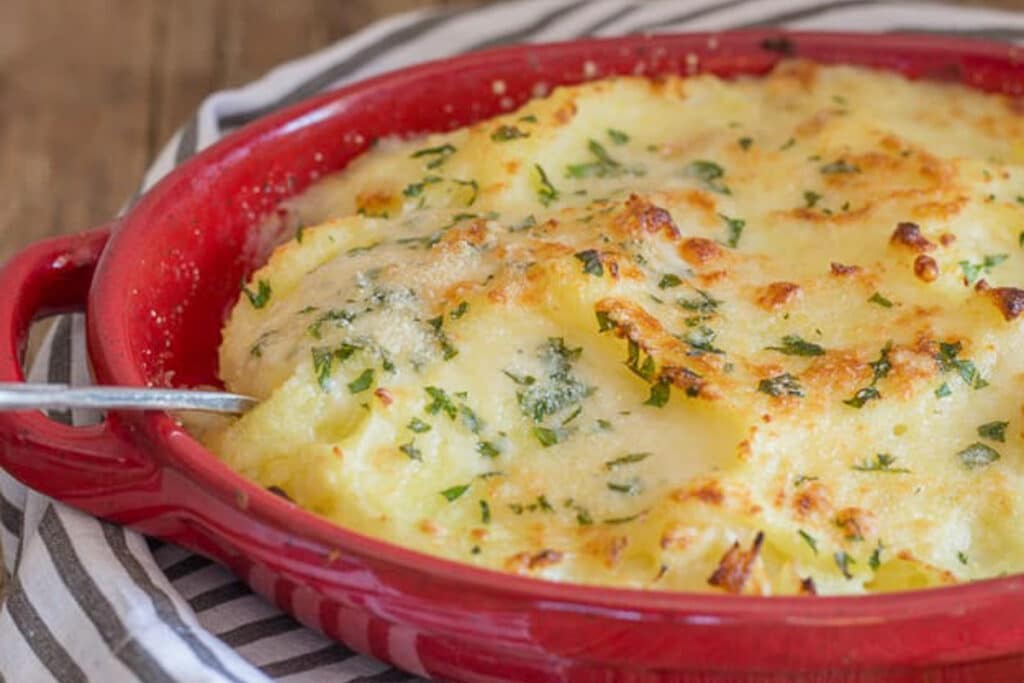 Mashed potato casserole in red dish with a silver spoon.